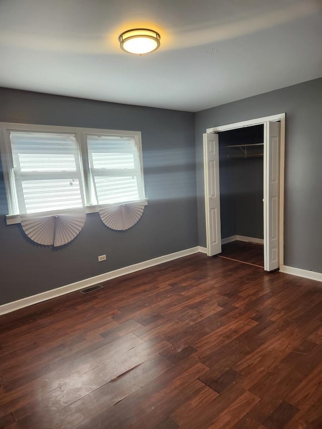 unfurnished bedroom with multiple windows, a closet, and dark hardwood / wood-style floors