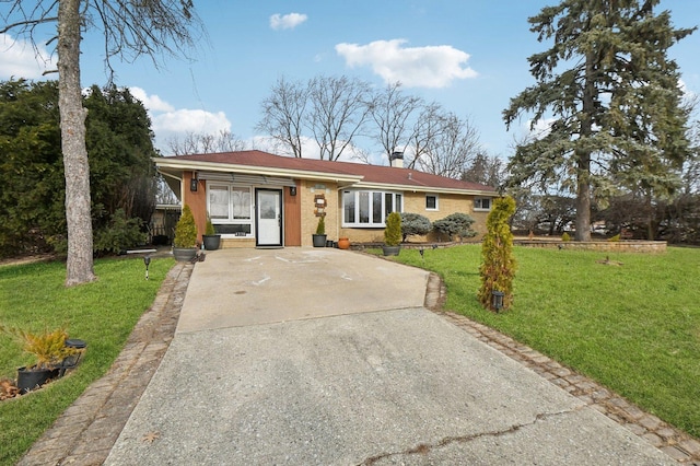 single story home with driveway, brick siding, a chimney, and a front lawn