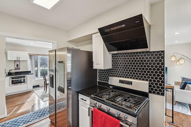 kitchen with tasteful backsplash, range hood, appliances with stainless steel finishes, light wood-style flooring, and white cabinetry