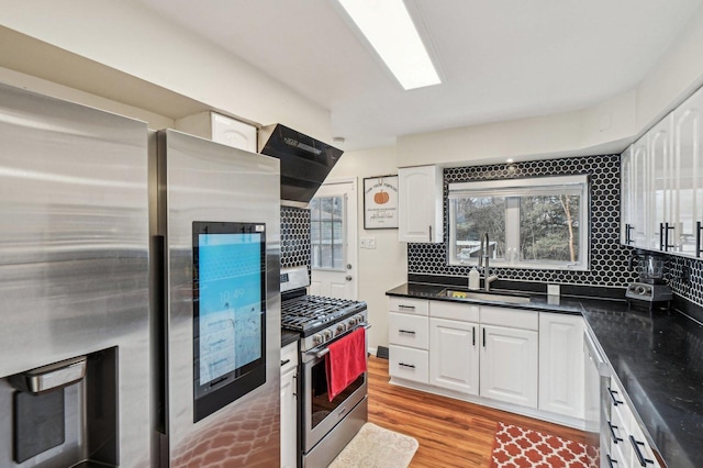 kitchen featuring dark countertops, extractor fan, appliances with stainless steel finishes, white cabinetry, and a sink