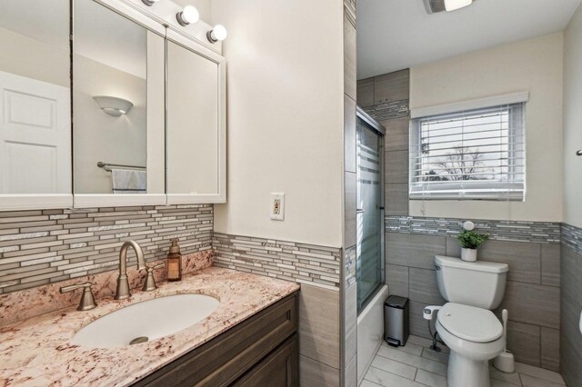 full bathroom with a wainscoted wall, toilet, tile walls, enclosed tub / shower combo, and vanity