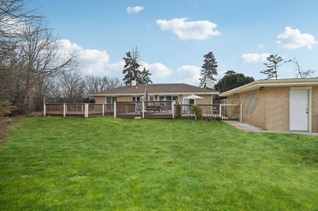 rear view of property with a deck, a yard, brick siding, and a chimney