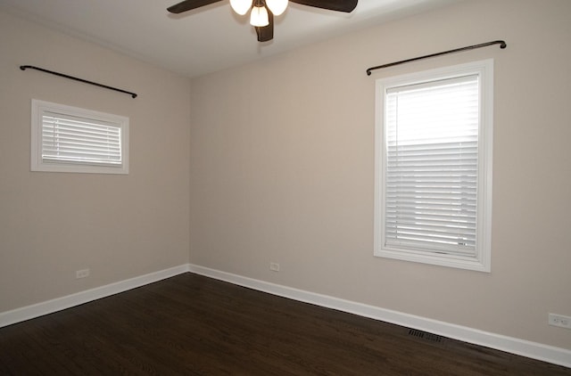 empty room featuring dark wood-style flooring, visible vents, ceiling fan, and baseboards