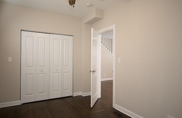 unfurnished bedroom featuring a closet, dark wood-style flooring, visible vents, and baseboards