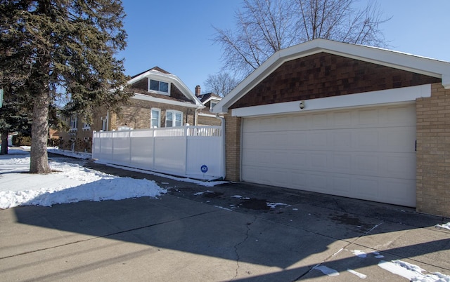 snow covered garage featuring a garage and fence