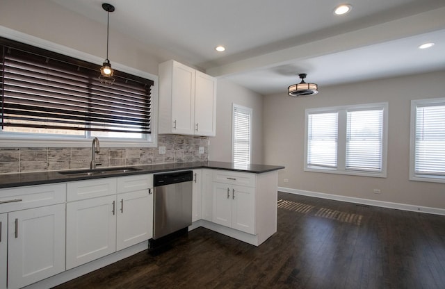 kitchen featuring white cabinets, dark countertops, hanging light fixtures, stainless steel dishwasher, and a sink