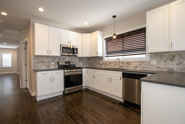 kitchen with stainless steel appliances, a sink, white cabinets, hanging light fixtures, and dark countertops