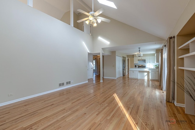 unfurnished living room with a ceiling fan, vaulted ceiling with skylight, visible vents, and light wood finished floors