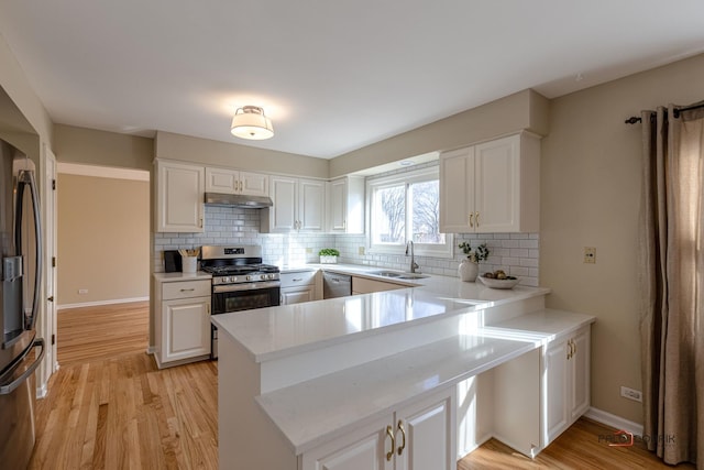 kitchen with white cabinets, appliances with stainless steel finishes, a peninsula, under cabinet range hood, and a sink