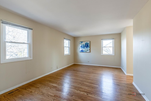 unfurnished room featuring visible vents, a wealth of natural light, and wood finished floors