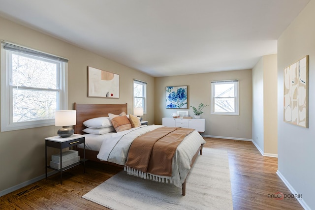 bedroom with multiple windows, visible vents, baseboards, and wood finished floors