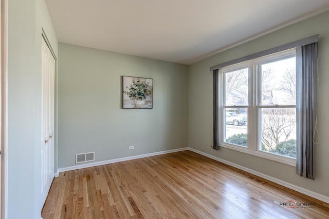 empty room with light wood-style flooring, plenty of natural light, visible vents, and baseboards