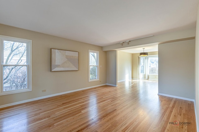 unfurnished room featuring light wood finished floors, a wealth of natural light, and baseboards