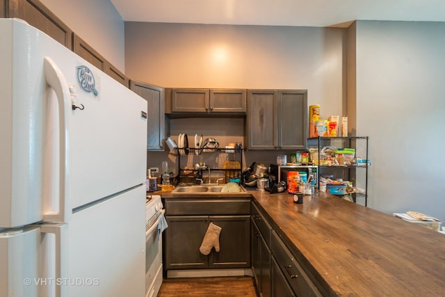 kitchen featuring white appliances, dark brown cabinetry, dark wood-type flooring, wood counters, and sink