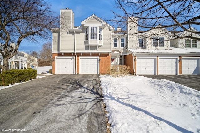 view of property with aphalt driveway, brick siding, a chimney, and a garage