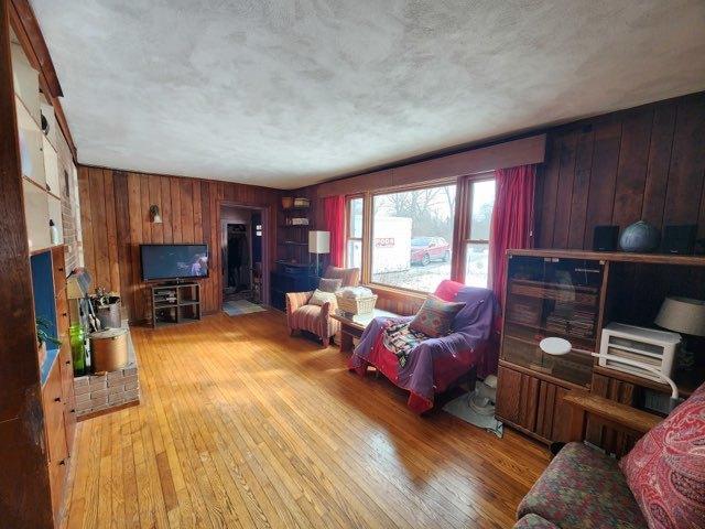 living area featuring light wood-type flooring, wood walls, and a textured ceiling