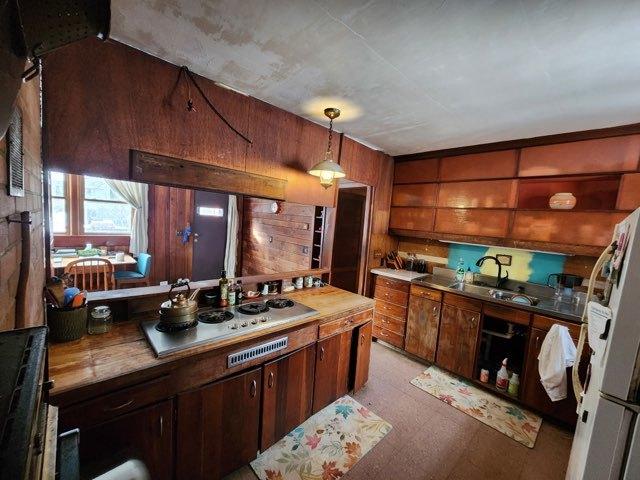 kitchen featuring wooden walls, freestanding refrigerator, stovetop, pendant lighting, and a sink