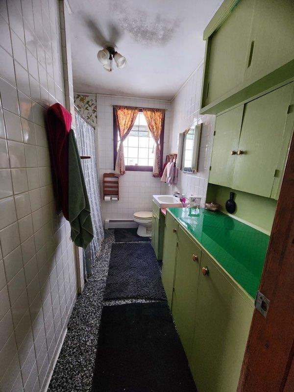 full bathroom featuring toilet, baseboard heating, vanity, and tile walls