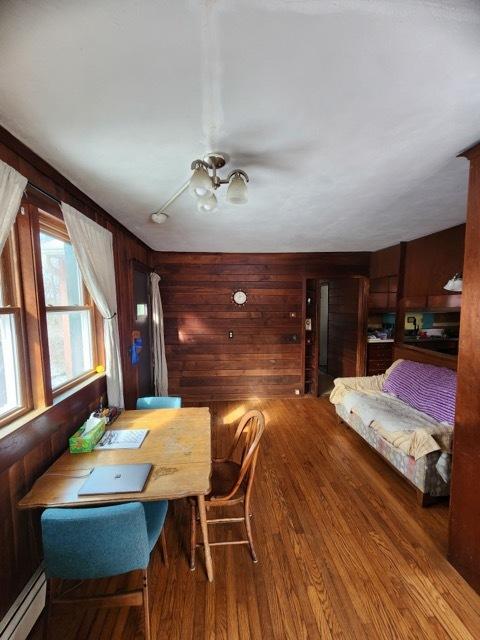 dining area featuring wooden walls, a baseboard heating unit, and wood finished floors