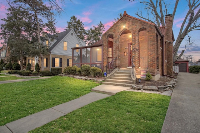 view of front of property with brick siding, a detached garage, a yard, a chimney, and an outdoor structure