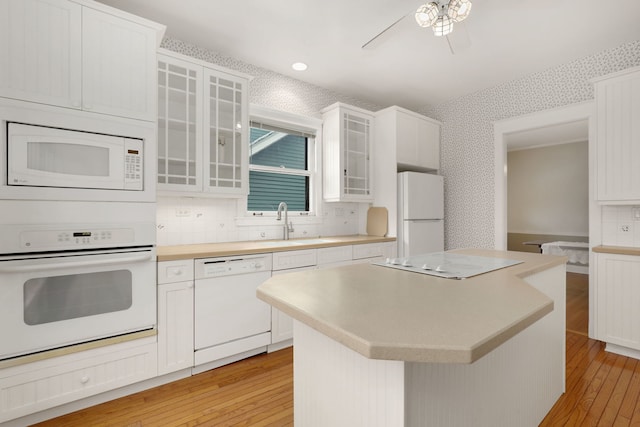 kitchen featuring light countertops, light wood-style flooring, a sink, white appliances, and wallpapered walls