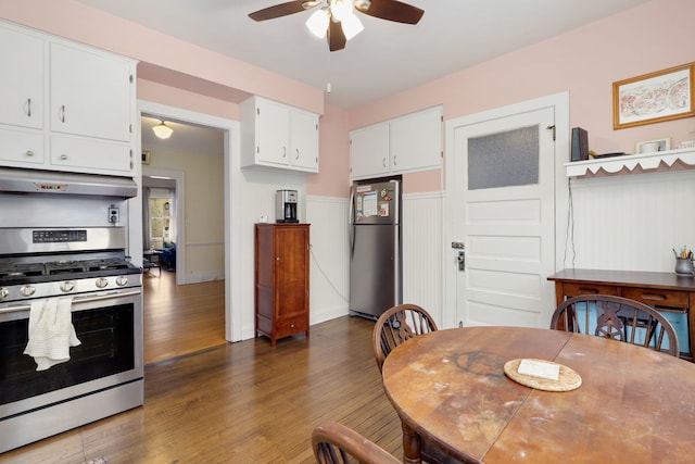 kitchen featuring appliances with stainless steel finishes, wainscoting, white cabinetry, wood finished floors, and under cabinet range hood