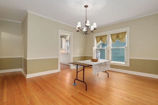 unfurnished dining area featuring baseboards, crown molding, light wood finished floors, and an inviting chandelier