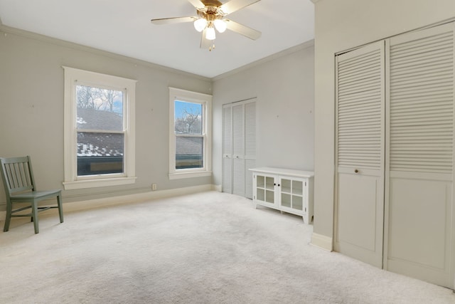 interior space with a ceiling fan, carpet, crown molding, and baseboards