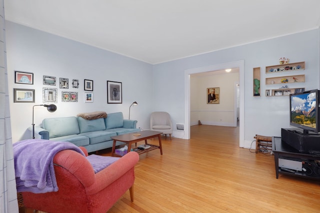 living room featuring crown molding, light wood finished floors, visible vents, and baseboards