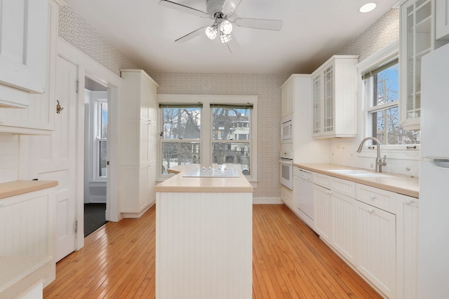 kitchen with light wood finished floors, wallpapered walls, white appliances, a center island, and a sink