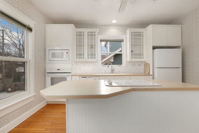 kitchen featuring light wood finished floors, light countertops, a sink, white appliances, and wallpapered walls