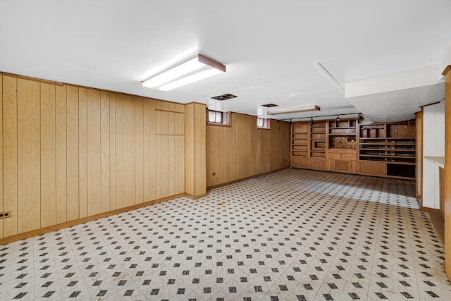 basement with baseboards, visible vents, wooden walls, and light floors