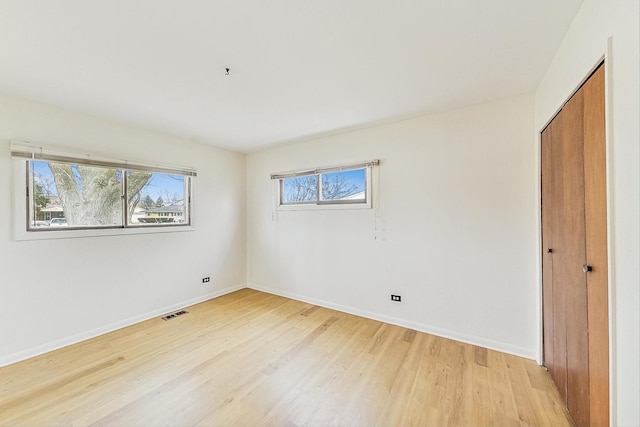 unfurnished bedroom featuring light wood-style flooring, a closet, visible vents, and baseboards