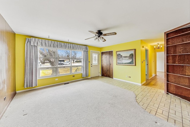 carpeted empty room featuring baseboards, visible vents, and ceiling fan with notable chandelier