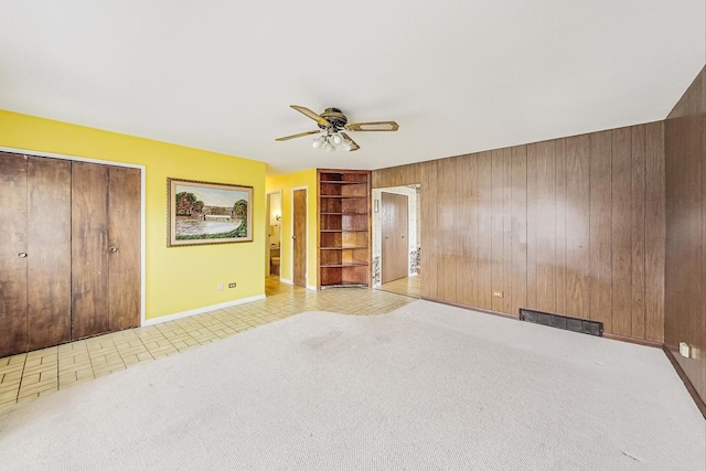 empty room with built in shelves, carpet, visible vents, a ceiling fan, and wood walls