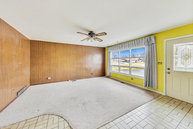 spare room with light colored carpet, wood walls, visible vents, and ceiling fan