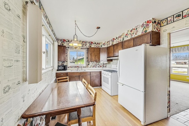 kitchen with light countertops, light wood-style flooring, a sink, white appliances, and under cabinet range hood