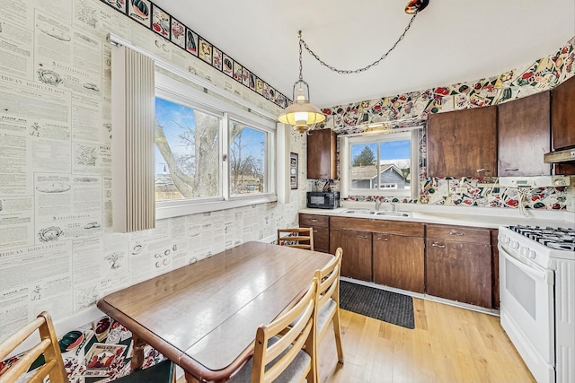 kitchen with pendant lighting, gas range gas stove, light wood finished floors, light countertops, and a sink