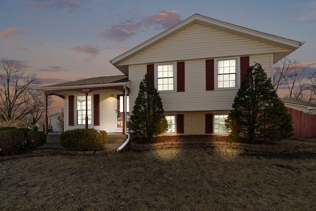 tri-level home featuring brick siding, covered porch, and a yard