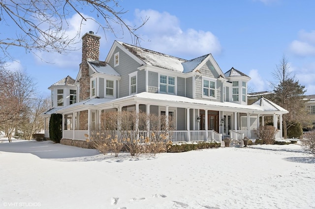 snow covered rear of property featuring covered porch and a chimney