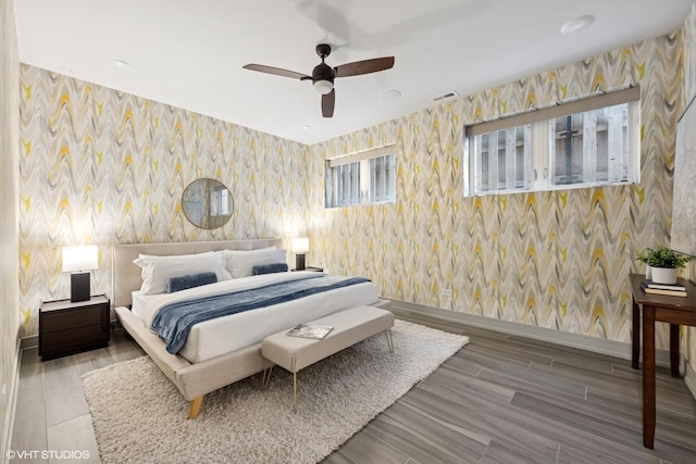 bedroom with ceiling fan, wood finished floors, visible vents, baseboards, and wallpapered walls