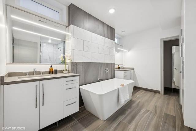 full bathroom with a freestanding tub, two vanities, a sink, a marble finish shower, and wood tiled floor