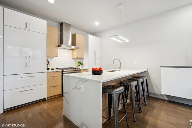 kitchen featuring a sink, a kitchen breakfast bar, white cabinets, hanging light fixtures, and wall chimney range hood