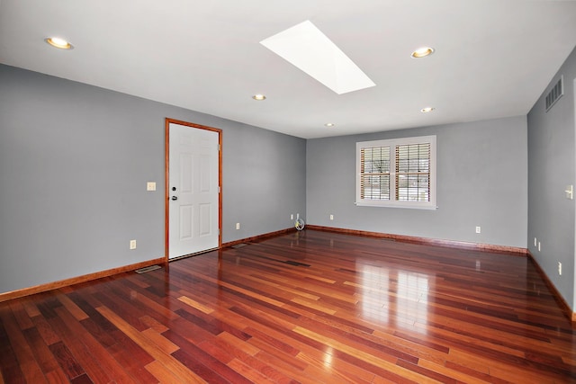 spare room featuring a skylight, wood finished floors, visible vents, and baseboards