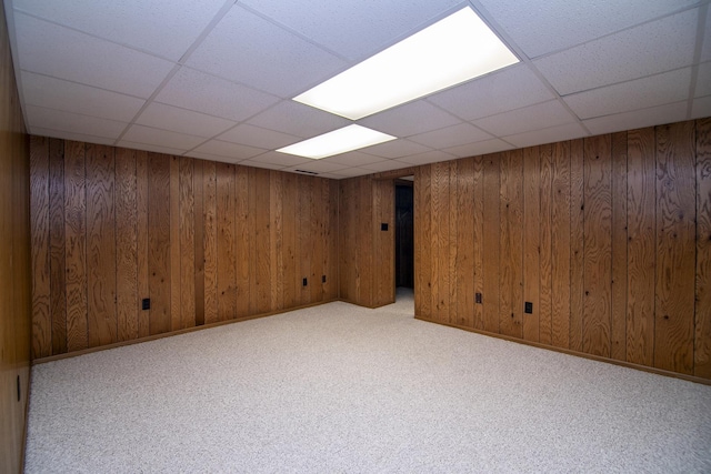 finished basement with light carpet, baseboards, a paneled ceiling, and wooden walls