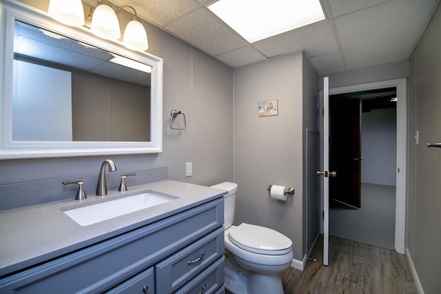 half bath with toilet, a paneled ceiling, wood finished floors, vanity, and baseboards