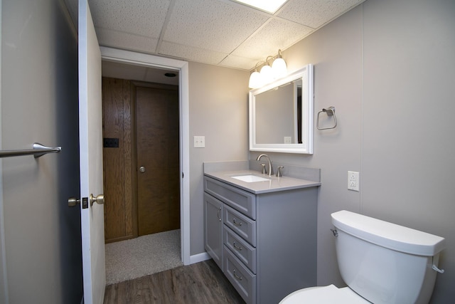 half bath featuring a paneled ceiling, toilet, wood finished floors, and vanity