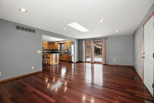 unfurnished living room featuring a skylight, baseboards, dark wood-style floors, and visible vents