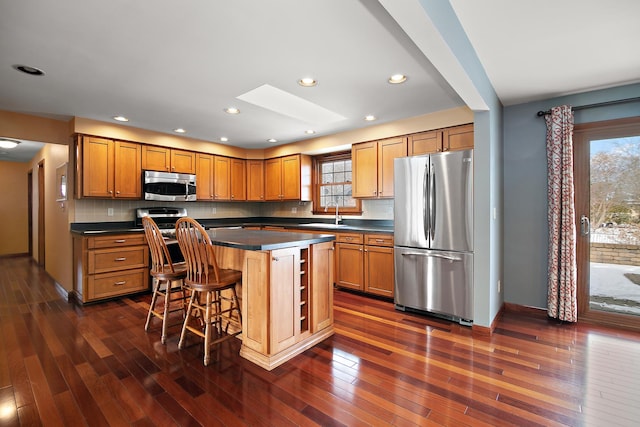 kitchen with a center island, a skylight, stainless steel appliances, dark countertops, and a kitchen breakfast bar