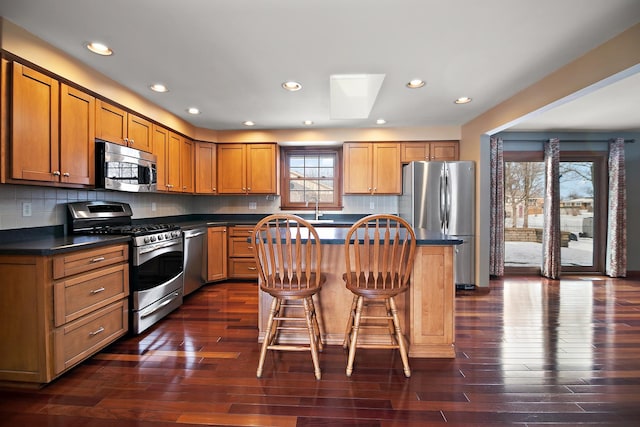 kitchen with a breakfast bar, a sink, a kitchen island, appliances with stainless steel finishes, and dark countertops